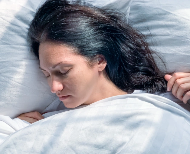 Woman sleeping peacefully on white pillows and bedding in bedroom setting.
